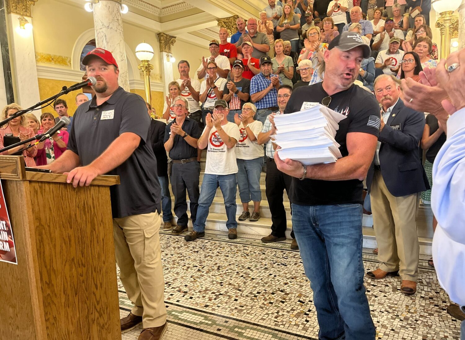Landowners Mark Lapka of McPherson County, left, and Jared Bossly of Brown County, holding petitions with about 2,000 signatures, speak at the state Capitol in Pierre on July 6, demanding a prohibition against carbon capture pipeline companies gaining access to land against a landowner’s will. South Dakota Searchlight photo by Joshua HaiarCarbon pipelines